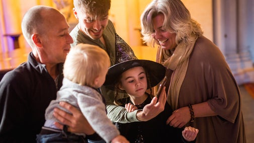 Family, including girl dressed as witch, laughing at a phone.